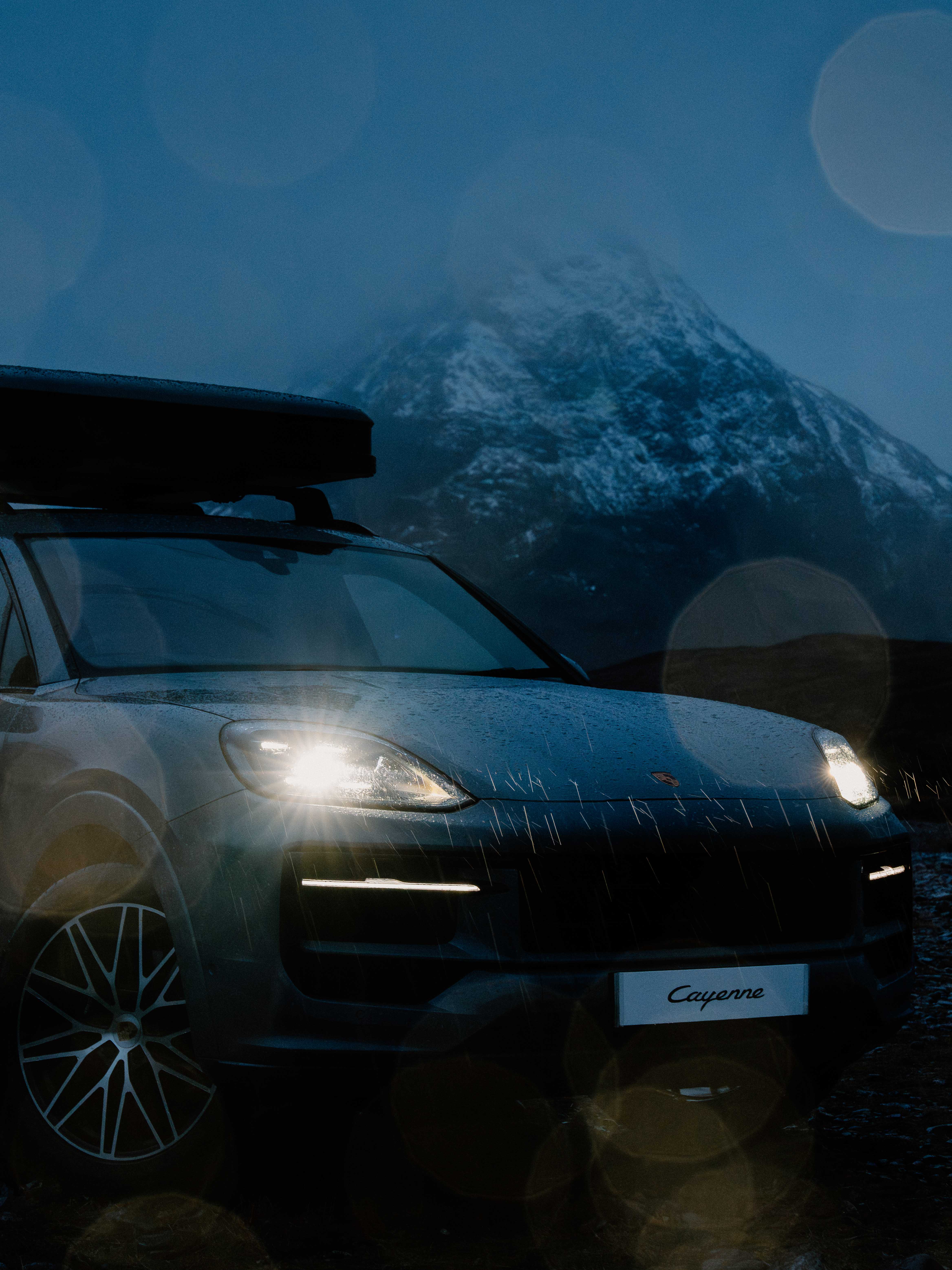 A Porsche in the rain with a snowy mountain in the background at dusk
